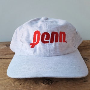 Op de afbeelding: Een grijze baseballpet met een rood geborduurd logo met de tekst "Penn".