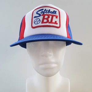 May include: A blue, red and white trucker hat with a white mesh back. The front of the hat has a red and blue embroidered patch that says "Softball BL".