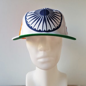 May include: A white baseball cap featuring a navy blue and white design on the crown, with a green brim. The cap has orange and green accents on the side, and is displayed on a mannequin head.
