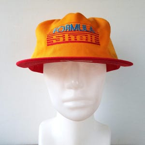 May include: A yellow and red trucker hat with a blue and red embroidered logo that says "Formula 1" on the front.