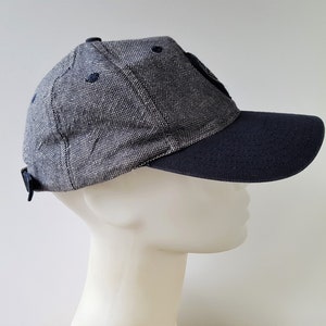 May include: A navy blue and gray baseball cap with a curved brim. The cap has a textured fabric and a small, dark patch on the front. The brim and the adjustable strap are navy blue.
