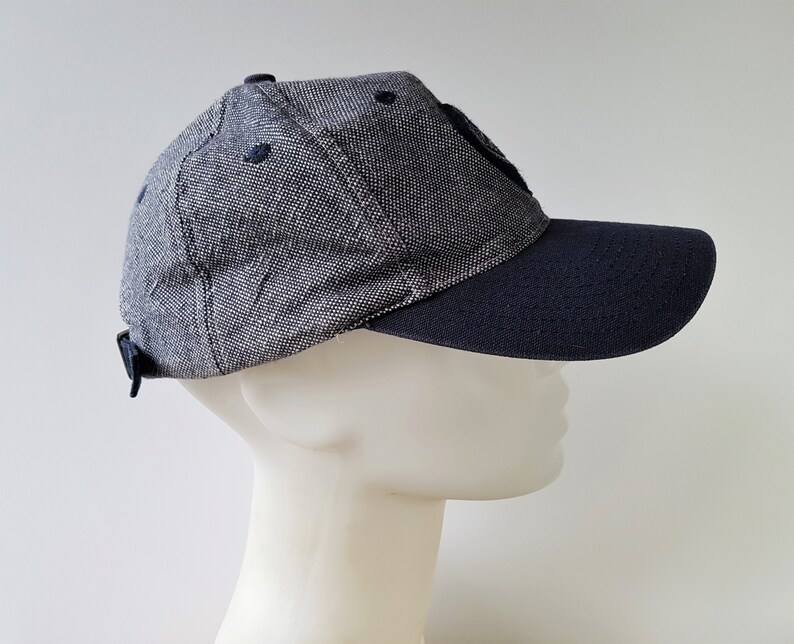 May include: A navy blue and gray baseball cap with a curved brim. The cap has a textured fabric and a small, dark patch on the front. The brim and the adjustable strap are navy blue.