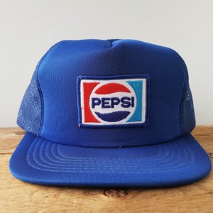 Pode incluir: Um chapéu de caminhoneiro de malha azul e branco com um logotipo Pepsi bordado em vermelho, branco e azul na frente.