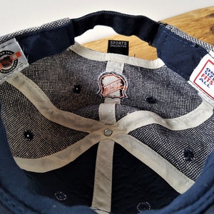 May include: Navy blue baseball cap with a white and gray patterned interior. The cap features the NHL logo and tags from Sports Specialties and Center Ice. The cap has a curved brim and a dark blue sweatband.