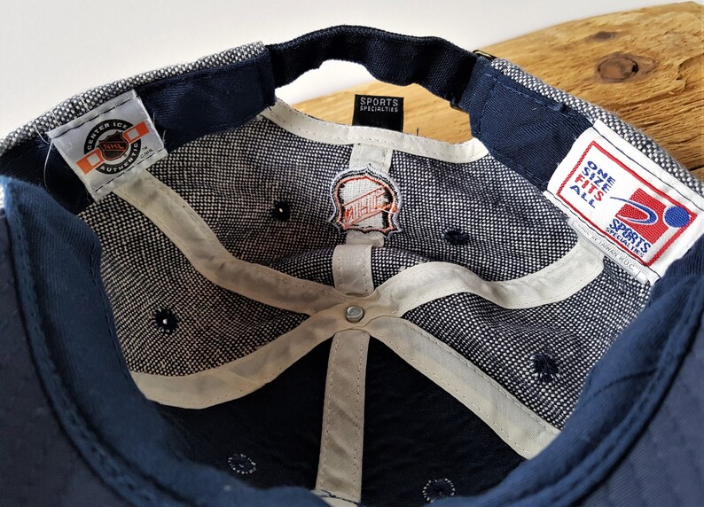 May include: Navy blue baseball cap with a white and gray patterned interior. The cap features the NHL logo and tags from Sports Specialties and Center Ice. The cap has a curved brim and a dark blue sweatband.