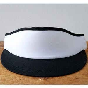 May include: A black and white visor with a wide brim. The visor is made of a soft, flexible material and has a black band around the top.