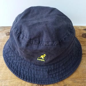K&ouml;nnte beinhalten: Ein marineblauer Fischerhut mit gelbem K&auml;nguru-Logo. Der Hut ist aus einem weichen Stoff gefertigt und hat eine klassische, abgerundete Form. Ein vielseitiges Accessoire f&uuml;r Sonnenschutz und Freizeitkleidung.