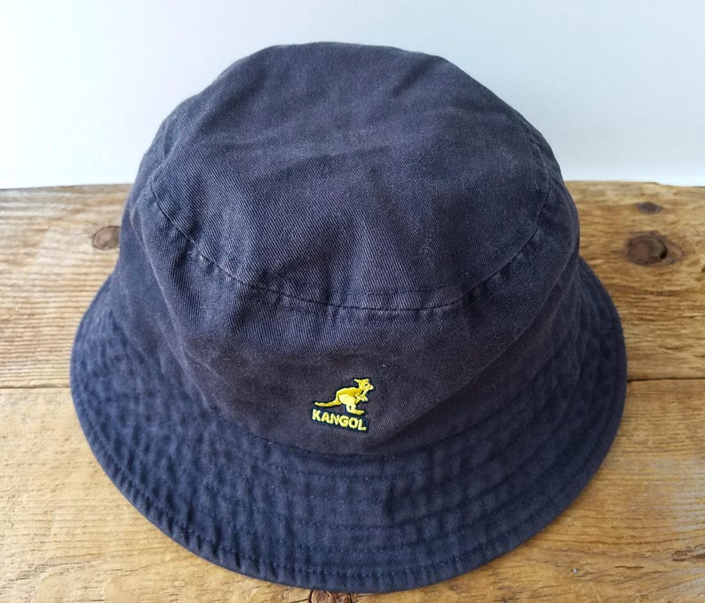 K&ouml;nnte beinhalten: Ein marineblauer Fischerhut mit gelbem K&auml;nguru-Logo. Der Hut ist aus einem weichen Stoff gefertigt und hat eine klassische, abgerundete Form. Ein vielseitiges Accessoire f&uuml;r Sonnenschutz und Freizeitkleidung.