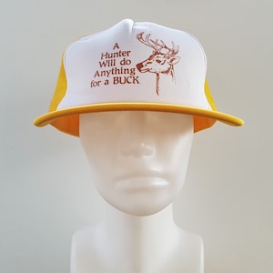 May include: A white and yellow trucker hat with a brown deer and the text "A Hunter Will do Anything for a BUCK".