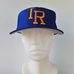 Puede incluir: Una gorra de béisbol azul real con visera blanca y un logotipo "IR" bordado en dorado.