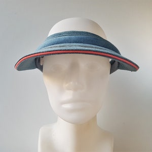 May include: A blue denim visor with a red trim. The visor is on a white mannequin head.