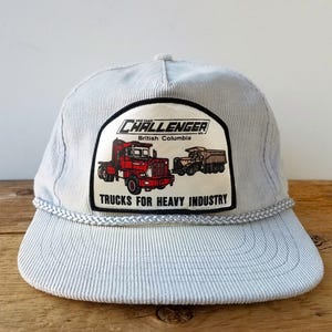 Puede incluir: Una gorra de béisbol de pana azul claro con un parche que muestra un camión semi-remolque rojo y blanco con el texto "The Great CHALLENGER British Columbia Trucks for Heavy Industry".