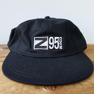 Può includere: Cappellino da baseball nero con un logo ricamato bianco che dice "Z95.3 FM".