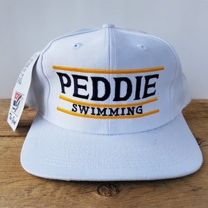 May include: White baseball cap with a black and gold embroidered logo that says "Peddie Swimming".