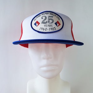 Könnte beinhalten: Weiße, rote und blaue Trucker-Kappe mit einem Patch, auf dem "Island Paper Mills Ltd. 25 Years 1960-1985" steht.
