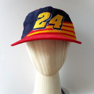 Puede incluir: Una gorra de béisbol azul marino con el número 24 en amarillo, contorneado en negro, en la parte delantera. La visera es roja y la gorra tiene rayas amarillas y rojas. La gorra se muestra en una cabeza de maniquí.