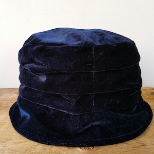 Peut inclure: Un chapeau seau en velours bleu marine avec un large bord et une couronne plissée.