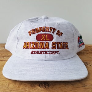 May include: Gray baseball cap with the text "PROPERTY OF ARIZONA STATE ATHLETIC DEPT." in red and yellow embroidery. The cap also has a small embroidered patch with a cartoon character.
