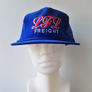 May include: A blue corduroy trucker hat with the text "LTL FREIGHT" embroidered in red and white. The hat features a mesh back and a braided rope detail along the brim.