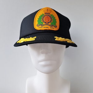 May include: Black baseball cap with a yellow and green embroidered patch that says "Royal Canadian Mounted Police High River, Alta."