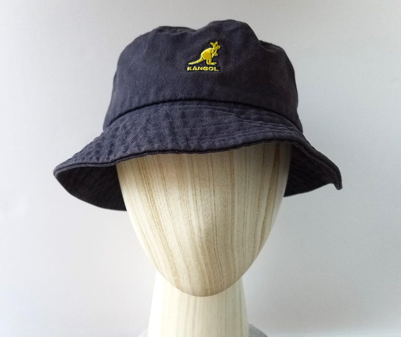 K&ouml;nnte beinhalten: Dunkelblauer Fischerhut mit gelbem K&auml;nguru-Logo. Der Hut hat ein leicht abgenutztes Aussehen und eine breite Krempe. Der Hut wird auf einem Schaufensterkopf pr&auml;sentiert. Durchmesser ca. 20 cm.