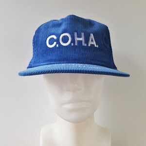 May include: A blue corduroy baseball cap with white embroidered text that reads "C.O.H.A."