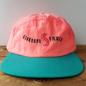 Puede incluir: Gorra color coral con visera turquesa. La gorra presenta el texto "GIORDANO SUMMER" en negro con un diseño de caballito de mar rojo. El sombrero es de material ligero, probablemente vintage.