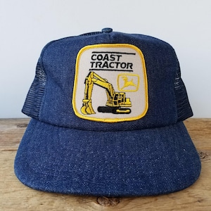 May include: A blue denim trucker hat with a yellow and black embroidered patch that says "Coast Tractor" and depicts a yellow excavator.