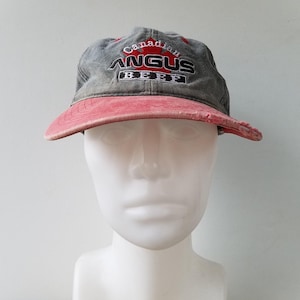 Pode incluir: Um boné de beisebol cinza e vermelho com o texto "Canadian Angus Beef" e um logotipo de folha de bordo vermelho.