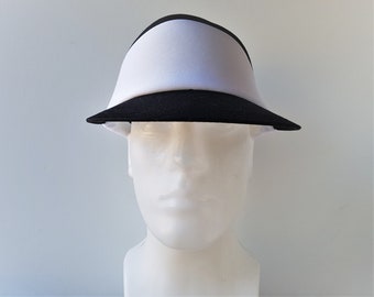 Könnte beinhalten: Ein schwarzer und weißer Visier mit breitem Schirm. Das Visier ist aus einem weichen, flexiblen Material gefertigt und hat ein weißes Band um die Oberseite.