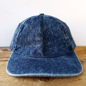 Può includere: Un berretto da baseball in denim blu con un aspetto leggermente rovinato. Il berretto ha una visiera curva e una corona strutturata.
