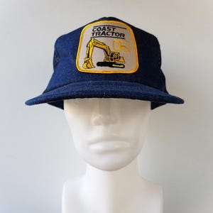 May include: A blue denim trucker hat with a yellow and black embroidered patch that says "Coast Tractor" and depicts a yellow excavator.