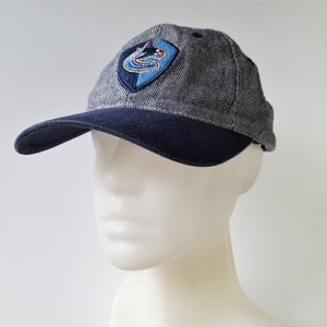 May include: A gray and navy blue baseball cap with a curved brim. The cap features a team logo patch on the front. The cap is made of a textured fabric and has a classic six-panel design.