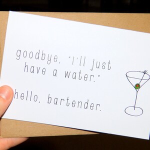 May include: A white greeting card with the text "goodbye, 'I'll just have a water.' hello, bartender." and a small drawing of a martini glass with an olive. The card is inside a brown envelope.