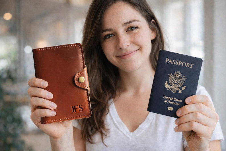 May include: A brown leather passport holder with the initials "JFS" and a navy blue United States passport. The passport holder has a button closure. The passport has the word "PASSPORT" on the cover.