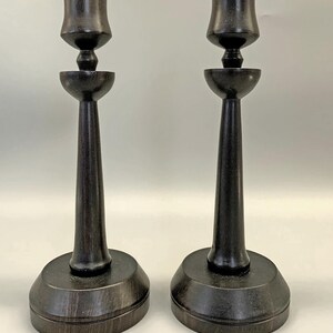 Pode incluir: Um par de casti&ccedil;ais de madeira castanho escuro com um design simples e elegante. Cada casti&ccedil;al tem uma base larga, um caule alto e fino e uma parte superior em forma de ta&ccedil;a.