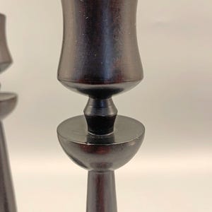 Pode incluir: Um par de casti&ccedil;ais de madeira preta com um design simples e elegante. Os casti&ccedil;ais t&ecirc;m uma base redonda e um caule alto e fino que se alarga na parte superior para formar uma ta&ccedil;a para a vela.