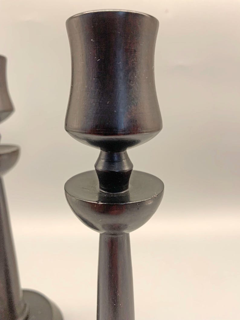 Pode incluir: Um par de casti&ccedil;ais de madeira preta com um design simples e elegante. Os casti&ccedil;ais t&ecirc;m uma base redonda e um caule alto e fino que se alarga na parte superior para formar uma ta&ccedil;a para a vela.