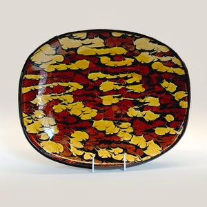 May include: A large, oval ceramic platter with a marbled glaze in shades of red, yellow, and black. The glaze creates a swirling pattern across the surface of the platter.