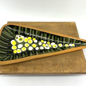 May include: A decorative, triangular ceramic dish with a wooden frame. The interior has a black background with green and white vertical lines, and yellow and white circular shapes.