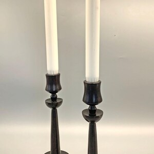 Pode incluir: Dois casti&ccedil;ais de madeira preta com velas brancas. Os casti&ccedil;ais t&ecirc;m um design simples e elegante com uma base redonda e um caule alto e fino.