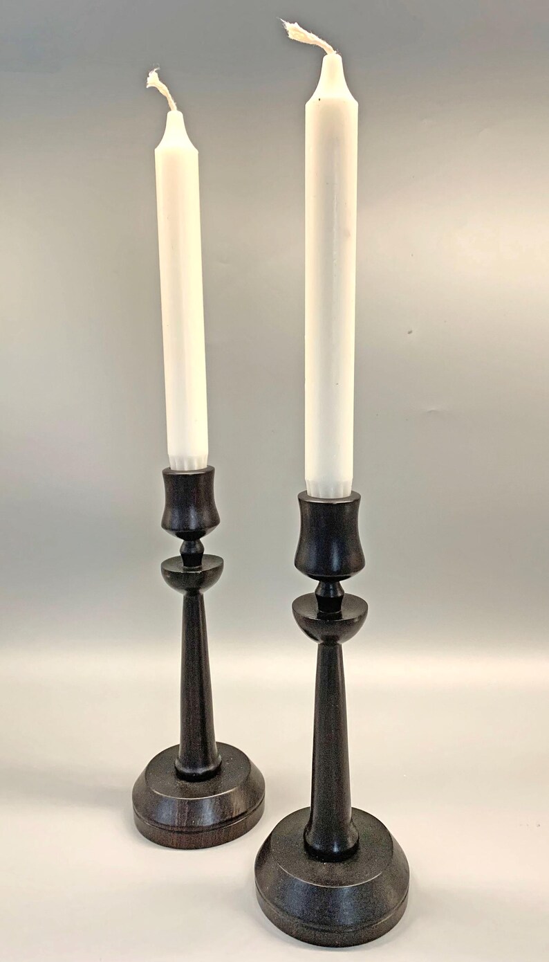 Pode incluir: Dois casti&ccedil;ais de madeira preta com velas brancas. Os casti&ccedil;ais t&ecirc;m um design simples e elegante com uma base redonda e um caule alto e fino.