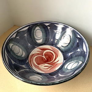 May include: A large, round ceramic bowl. The exterior is dark blue with overlapping oval shapes in shades of blue and white. The interior has a smaller, circular design in red and white. The bowl is suitable for serving. The diameter is approximately 30 cm.