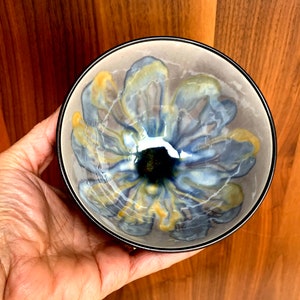 May include: A small ceramic bowl with a blue and yellow floral design. The bowl has a dark grey rim and a glossy finish.