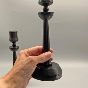 Pode incluir: Dois casti&ccedil;ais de madeira preta com um design simples. Os casti&ccedil;ais s&atilde;o altos e finos com uma base redonda. A parte superior do casti&ccedil;al &eacute; uma abertura em forma de ta&ccedil;a para uma vela.