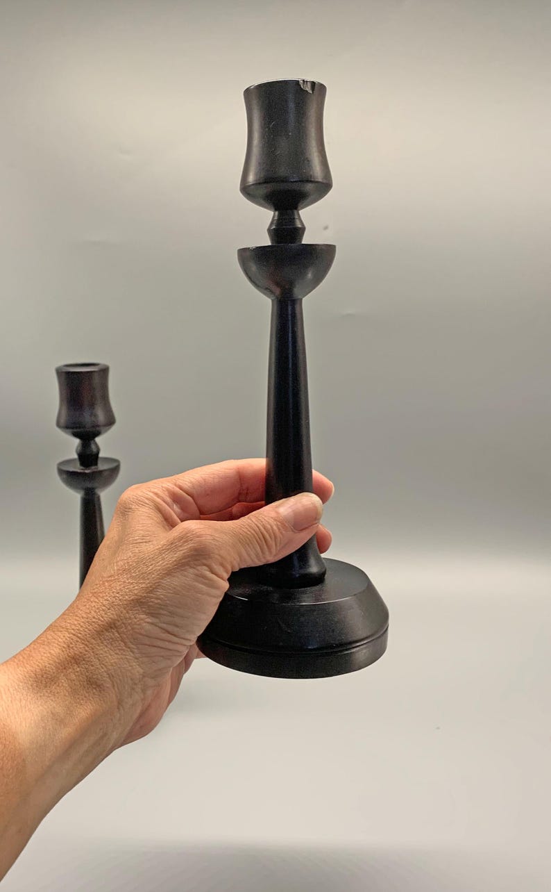 Pode incluir: Dois casti&ccedil;ais de madeira preta com um design simples. Os casti&ccedil;ais s&atilde;o altos e finos com uma base redonda. A parte superior do casti&ccedil;al &eacute; uma abertura em forma de ta&ccedil;a para uma vela.