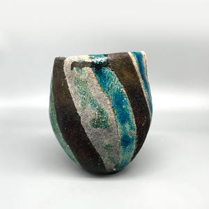 May include: A small, ceramic vase with a rounded shape and a swirling pattern of blue, green, brown, and white glaze.