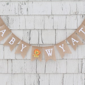 Pode incluir: Uma faixa de juta com as palavras "Baby Wyatt" em letras brancas. Um pequeno aplique de le&atilde;o est&aacute; entre o "y" e o "W".