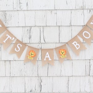 May include: A burlap banner with the words "It's a Boy" in white letters. The banner has small lion illustrations on some of the flags.