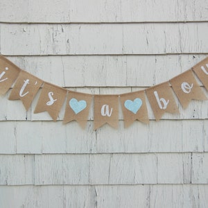 May include: A burlap banner with the words "it's a boy" in white lettering. The banner has two light blue hearts.
